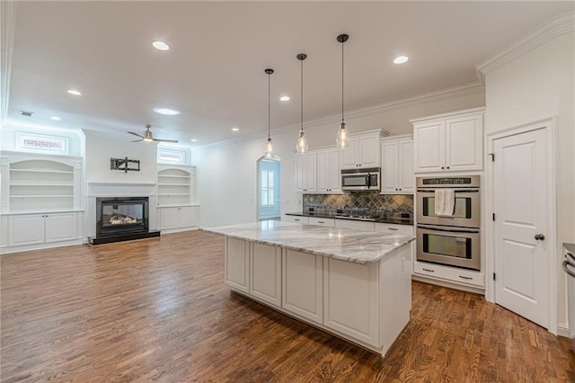 kitchen featuring appliances with stainless steel finishes, white cabinetry, pendant lighting, a kitchen island, and light stone countertops