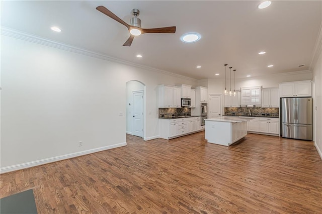 kitchen with white cabinetry, hanging light fixtures, a center island, ornamental molding, and appliances with stainless steel finishes