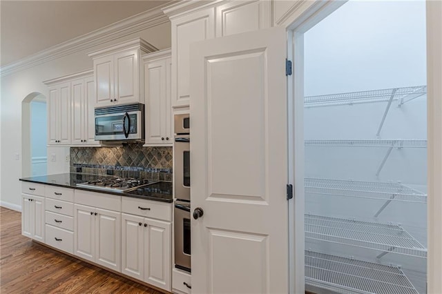 kitchen featuring white cabinetry, crown molding, stainless steel appliances, dark wood-type flooring, and decorative backsplash