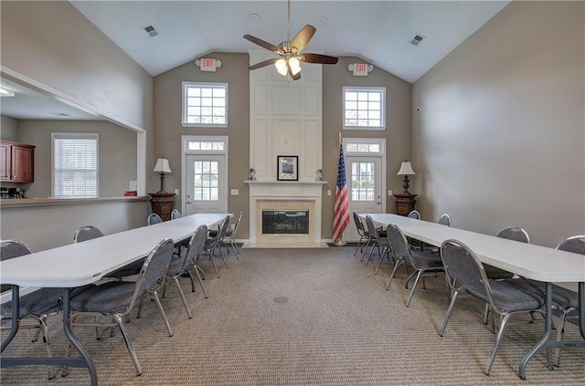 carpeted dining area featuring ceiling fan, a large fireplace, high vaulted ceiling, and a healthy amount of sunlight