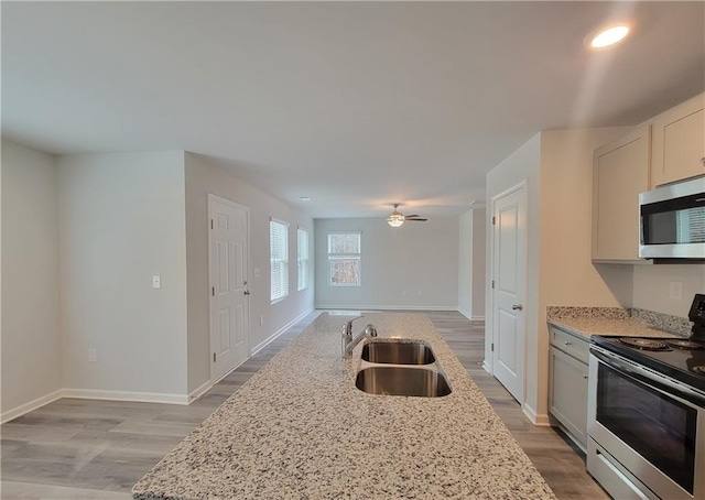 kitchen with sink, light stone counters, appliances with stainless steel finishes, ceiling fan, and white cabinets