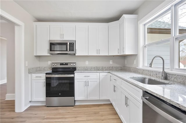 kitchen with light stone countertops, a sink, stainless steel appliances, light wood-style floors, and white cabinets