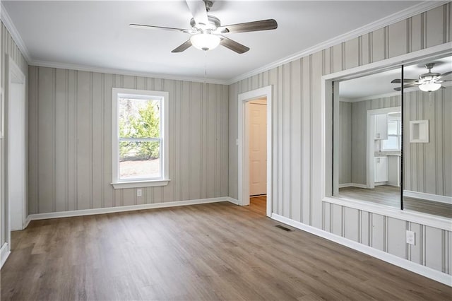 interior space featuring visible vents, baseboards, a closet, ornamental molding, and wood finished floors