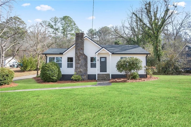 view of front facade with a front lawn, roof with shingles, entry steps, and a chimney