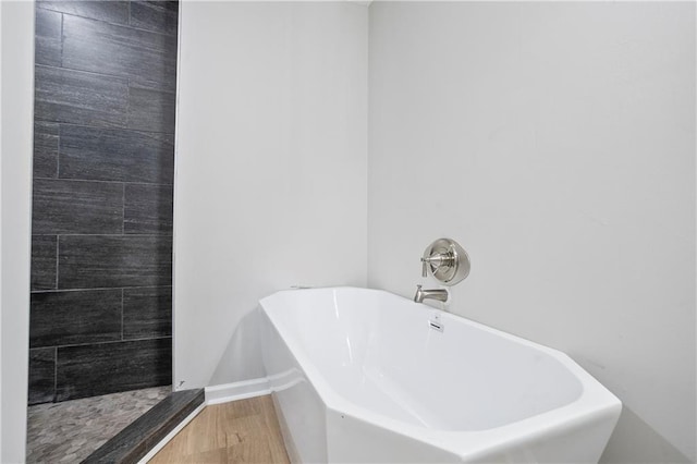 bathroom featuring wood finished floors, a soaking tub, a tile shower, and baseboards