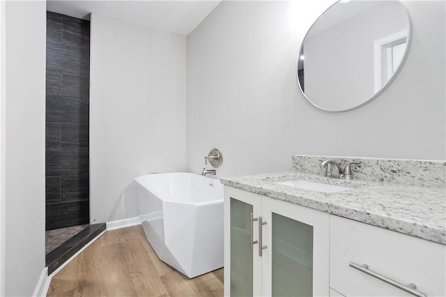 full bathroom with vanity, wood finished floors, a soaking tub, and baseboards