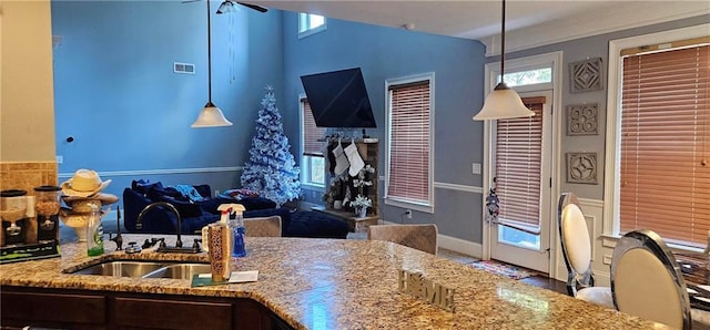 kitchen with decorative light fixtures, light stone countertops, sink, and a wealth of natural light