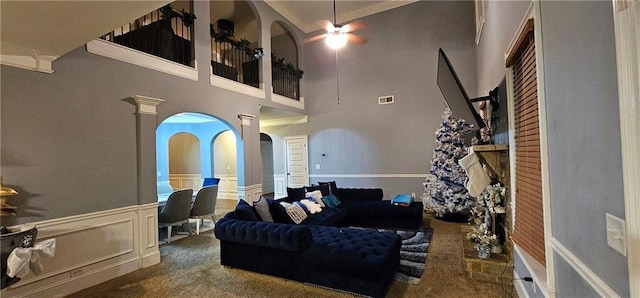 living room with ceiling fan, a towering ceiling, and dark carpet