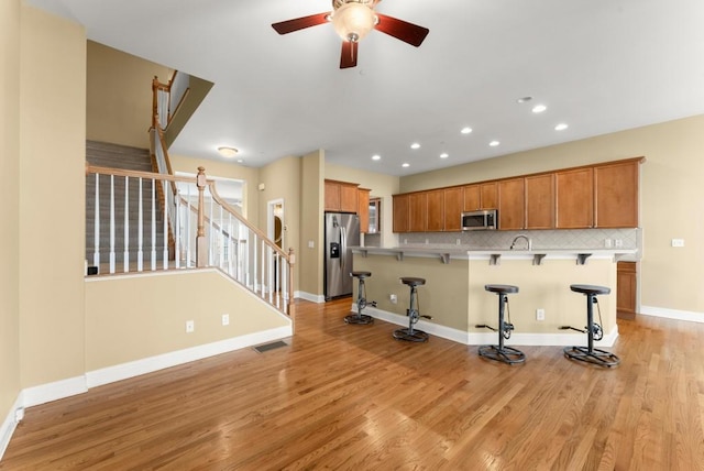 kitchen featuring light wood finished floors, tasteful backsplash, visible vents, a kitchen breakfast bar, and stainless steel appliances