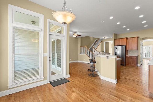 kitchen with ceiling fan, a kitchen island with sink, a breakfast bar, light wood-type flooring, and stainless steel refrigerator with ice dispenser