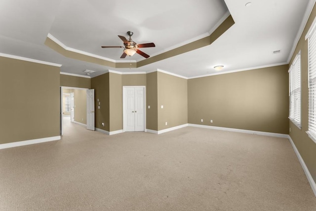 unfurnished room with baseboards, a raised ceiling, a ceiling fan, light colored carpet, and ornamental molding