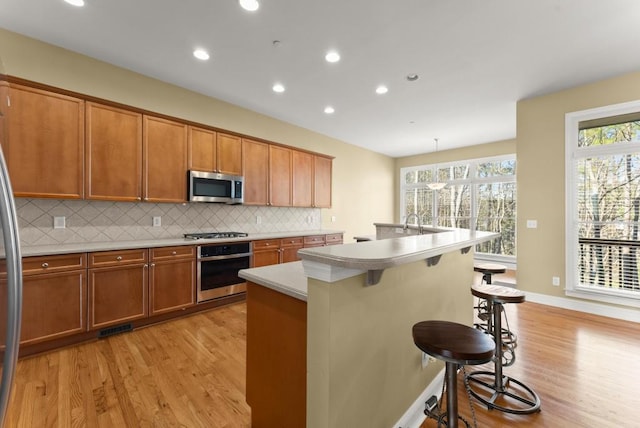 kitchen with appliances with stainless steel finishes, brown cabinetry, light wood-style flooring, and a kitchen breakfast bar