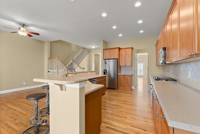 kitchen with stainless steel appliances, light wood finished floors, light countertops, and a large island with sink