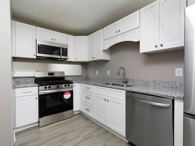 kitchen with white cabinetry, sink, stainless steel appliances, a textured ceiling, and light wood-type flooring