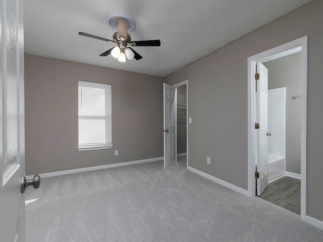 unfurnished bedroom featuring ensuite bath, ceiling fan, light colored carpet, and a textured ceiling