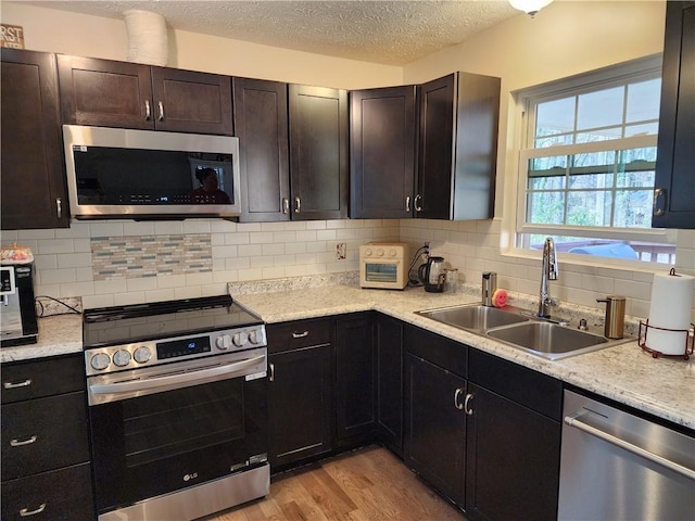 kitchen with appliances with stainless steel finishes, decorative backsplash, a sink, and light wood-style floors