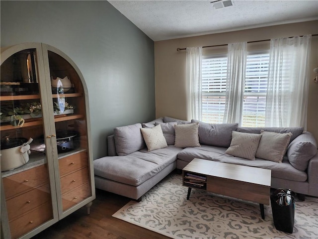 living room featuring vaulted ceiling, visible vents, dark wood finished floors, and a textured ceiling