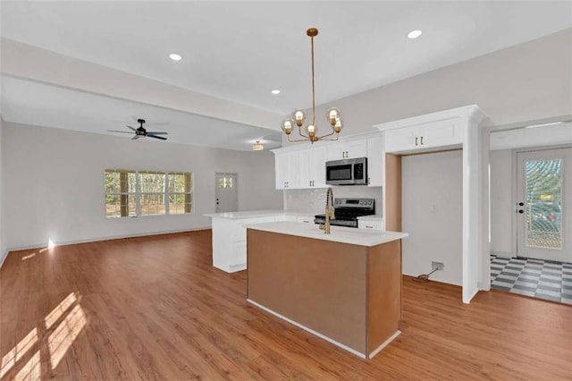 kitchen with a center island with sink, light countertops, light wood-style flooring, appliances with stainless steel finishes, and white cabinetry