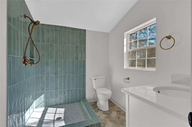 bathroom featuring toilet, lofted ceiling, a tile shower, and vanity