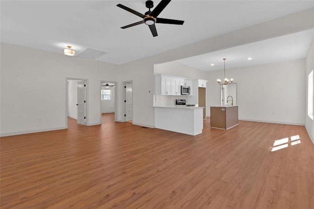 unfurnished living room with ceiling fan with notable chandelier, light wood-type flooring, a sink, and attic access