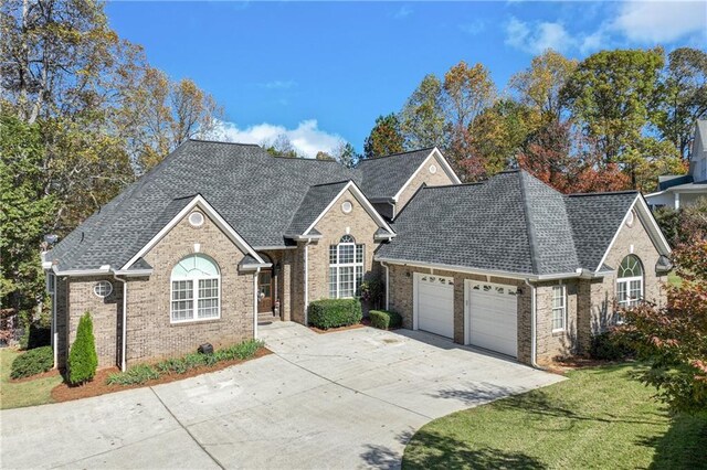 view of front of house with brick siding, a shingled roof, a front lawn, a garage, and driveway