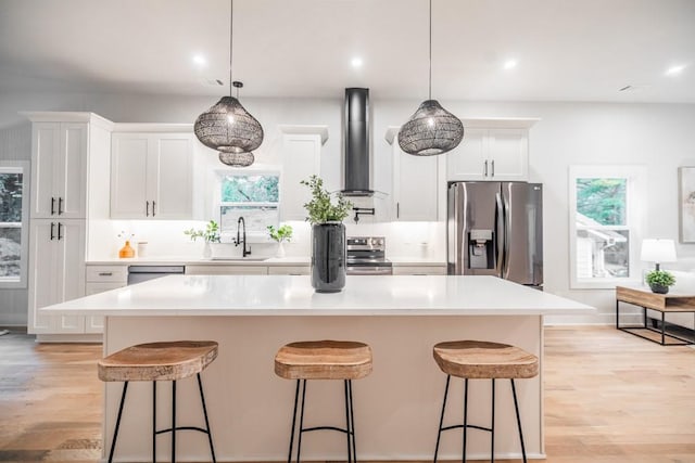 kitchen with stainless steel appliances, sink, a center island, white cabinets, and wall chimney range hood