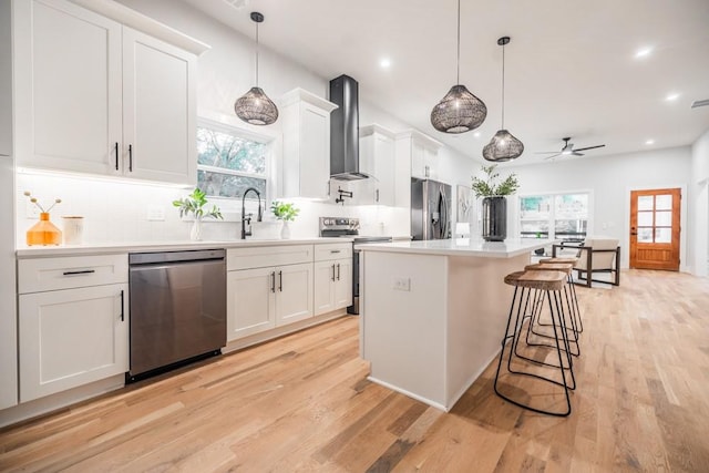 kitchen featuring white cabinetry, stainless steel appliances, a healthy amount of sunlight, and wall chimney range hood