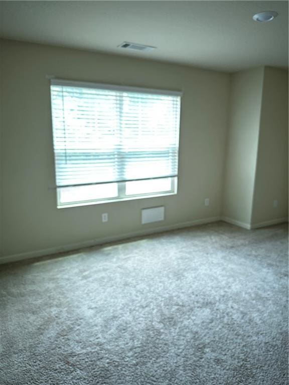 carpeted spare room with baseboards, visible vents, and a wealth of natural light