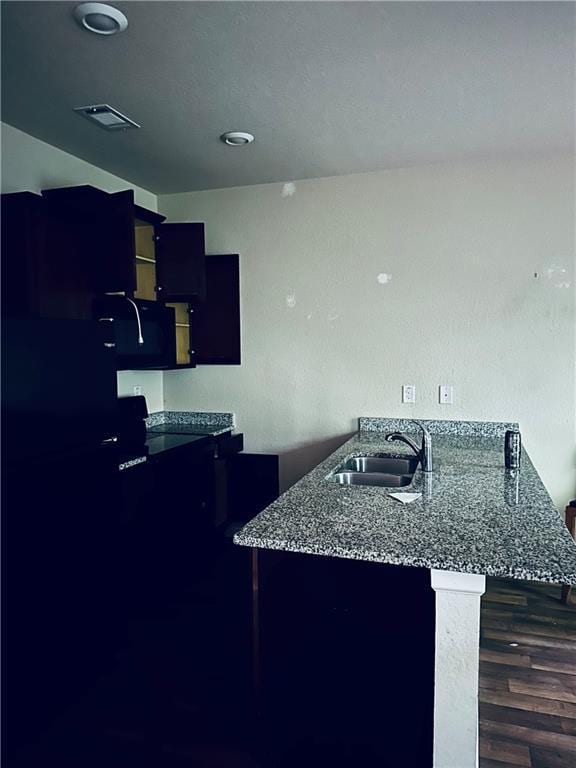 kitchen featuring visible vents, a sink, dark wood-style flooring, and a peninsula
