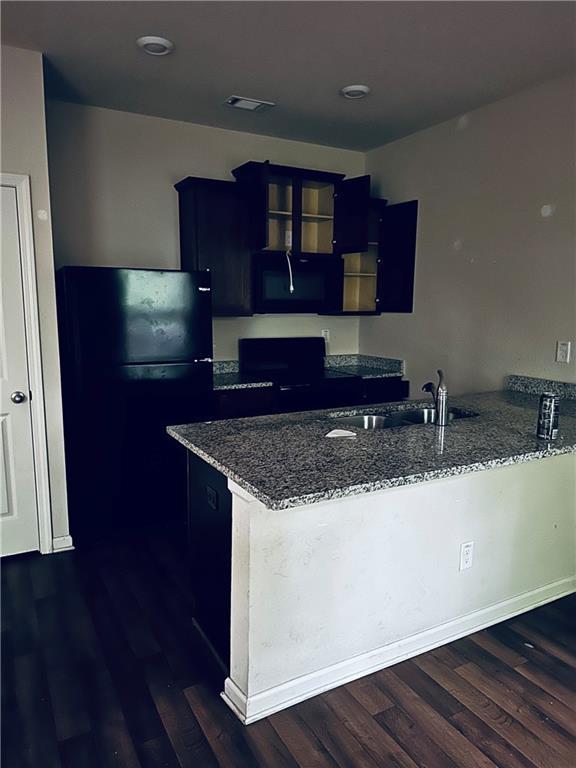 kitchen with blue cabinetry, a sink, stone countertops, black appliances, and a peninsula