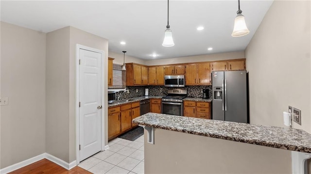 kitchen featuring stone countertops, kitchen peninsula, pendant lighting, stainless steel appliances, and backsplash