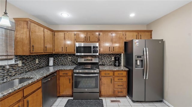 kitchen with sink, hanging light fixtures, dark stone countertops, appliances with stainless steel finishes, and decorative backsplash