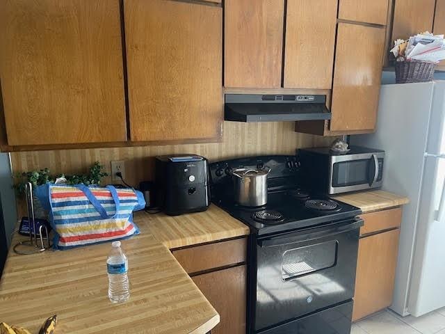 kitchen featuring black range with electric cooktop, light tile patterned floors, and white refrigerator