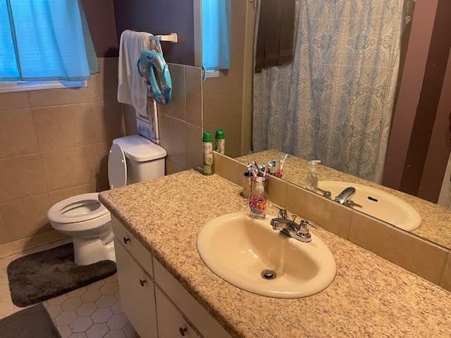 bathroom featuring toilet, curtained shower, vanity, and tile walls