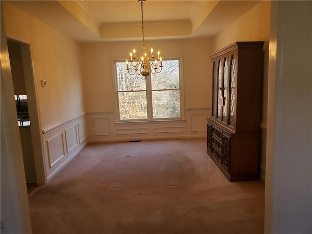 unfurnished dining area with a raised ceiling, carpet floors, and a chandelier