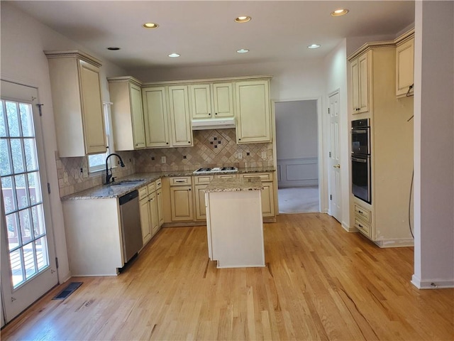 kitchen featuring sink, appliances with stainless steel finishes, plenty of natural light, light stone counters, and a kitchen island