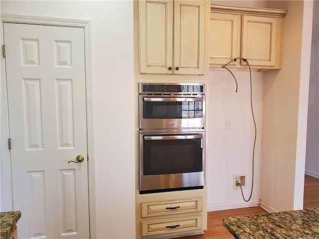 kitchen featuring cream cabinetry, double oven, dark stone counters, and light wood-type flooring