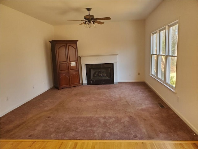 unfurnished living room with hardwood / wood-style flooring, a premium fireplace, a healthy amount of sunlight, and ceiling fan