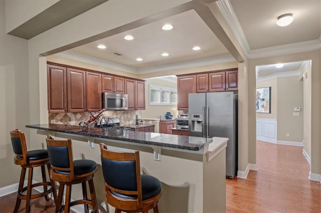 kitchen with tasteful backsplash, appliances with stainless steel finishes, light wood-type flooring, a peninsula, and a kitchen breakfast bar