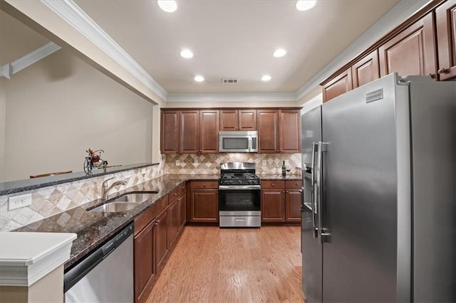 kitchen featuring appliances with stainless steel finishes, dark stone countertops, a sink, and crown molding