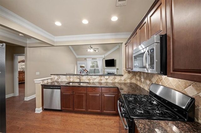 kitchen with light wood-style flooring, dark stone countertops, a sink, stainless steel appliances, and backsplash