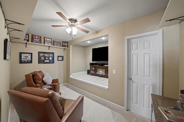 interior space featuring a glass covered fireplace, light carpet, ceiling fan, and baseboards