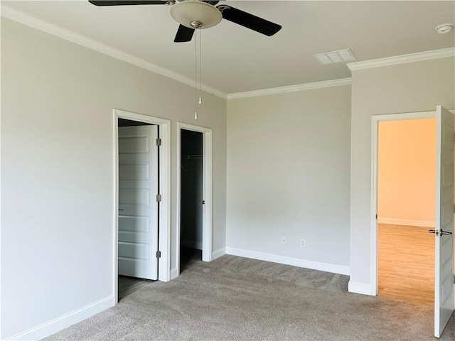 unfurnished bedroom with a walk in closet, ceiling fan, crown molding, and light colored carpet