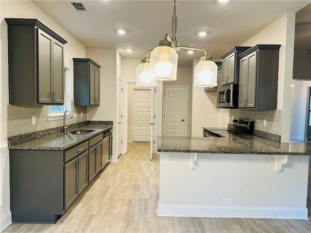 kitchen with a kitchen bar, light wood-type flooring, stainless steel appliances, sink, and pendant lighting