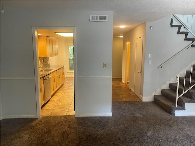 kitchen featuring light colored carpet, a textured ceiling, light brown cabinets, and stainless steel dishwasher