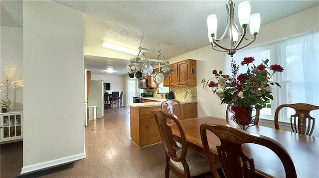 dining room featuring a textured ceiling, an inviting chandelier, plenty of natural light, and dark wood-type flooring