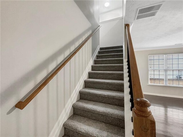 stairs featuring visible vents, crown molding, baseboards, wood finished floors, and a textured ceiling