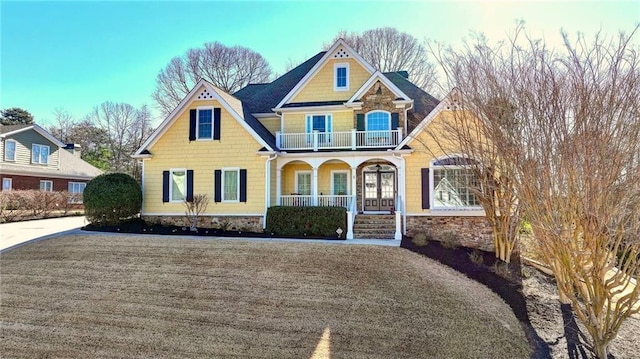 view of front of property with a balcony, stone siding, driveway, and a porch