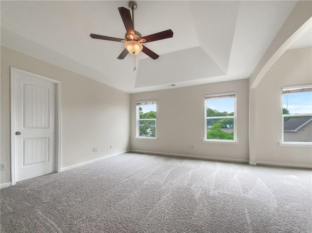 carpeted empty room featuring plenty of natural light, a raised ceiling, and ceiling fan