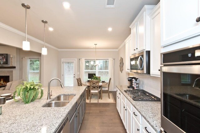 kitchen featuring white cabinets, stainless steel appliances, hanging light fixtures, and a center island with sink